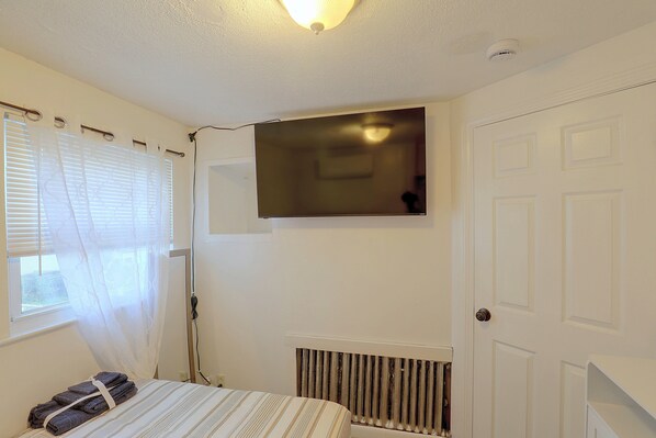 A room with a bed, a radiator, a door, and a window with blinds.