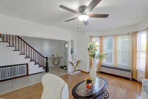 A spacious living room with a wooden staircase, a ceiling fan, and a large window with curtains.