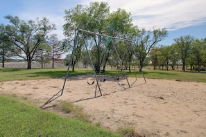A park with a swing set, trees, and a sandy ground.