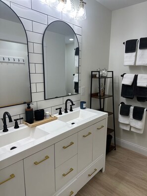 Ein modernes Badezimmer mit einem Doppelwaschbecken, schwarzen Wasserhähnen, einem großen Spiegel und einem Handtuchhalter.
