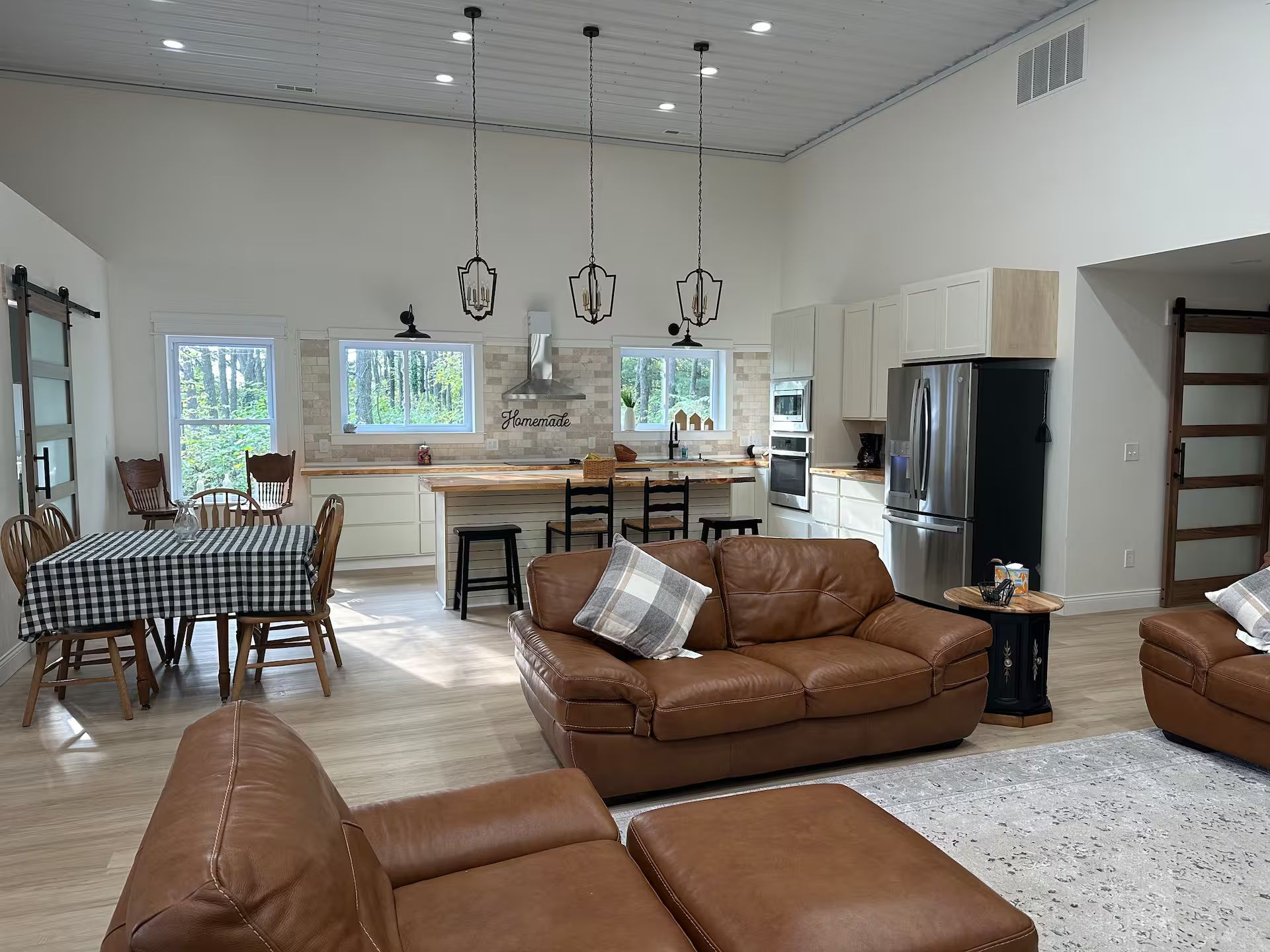 Ein geräumiges Wohnzimmer mit einem braunen Ledersofa und Hocker, ein Essbereich mit kariertem Tischleintuch und eine Küche mit modernen Geräten.