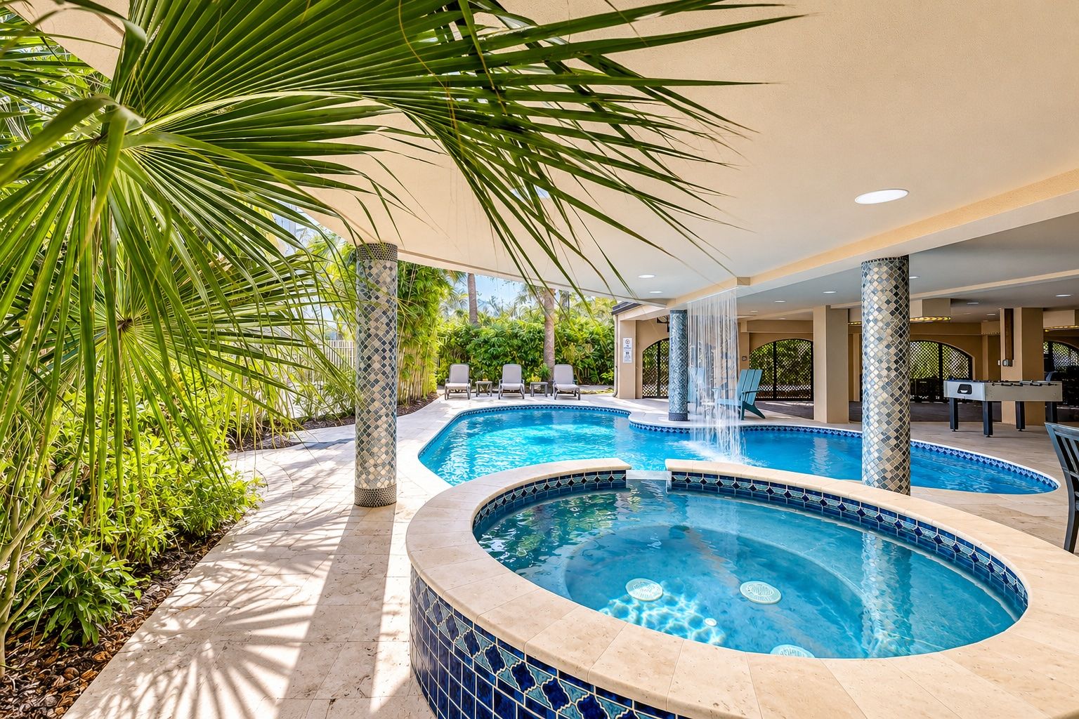 Zona de piscina con hidromasaje, sillas de descanso y una cascada.