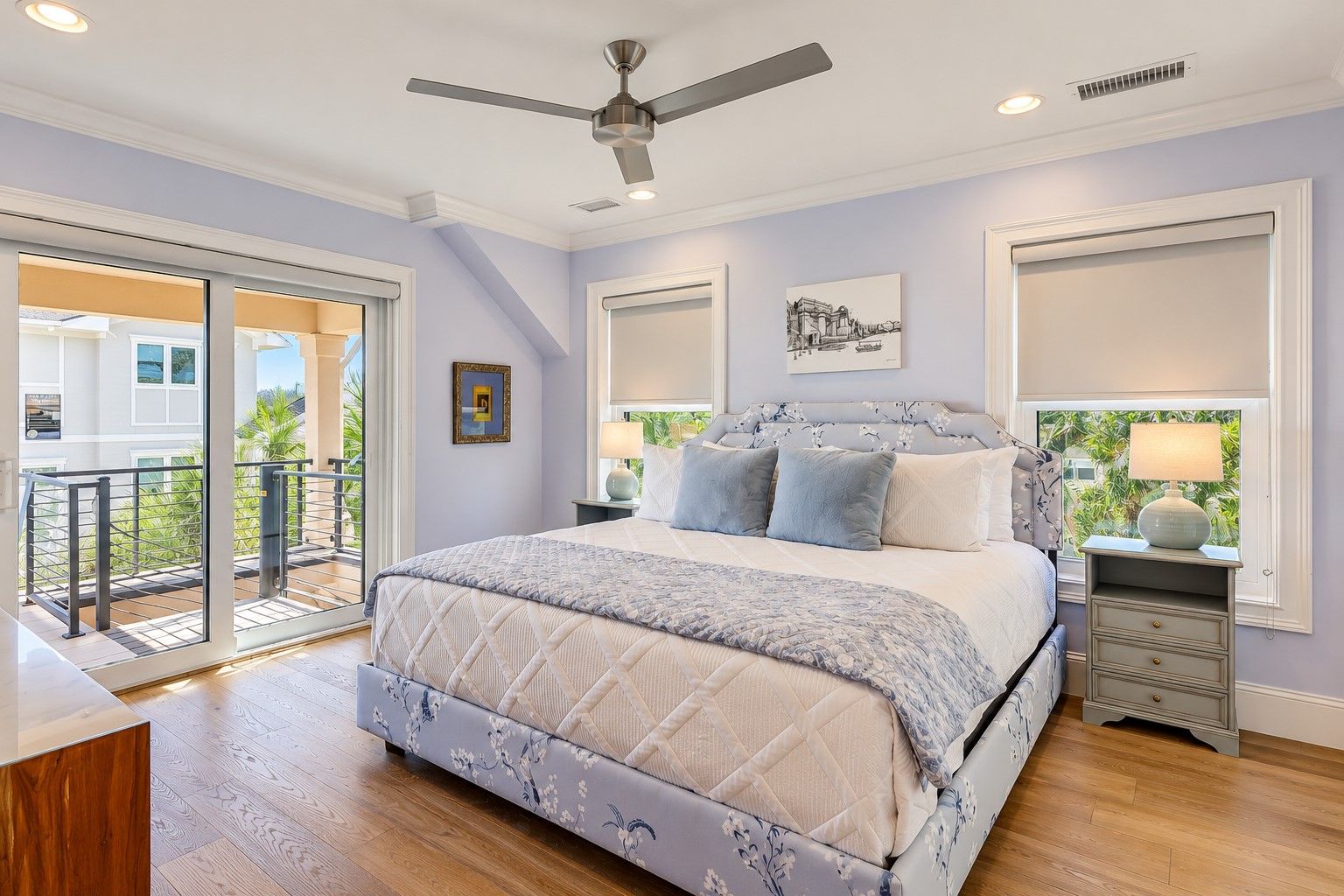 A bedroom with a bed, a ceiling fan, a nightstand, a lamp, and a window with a view.