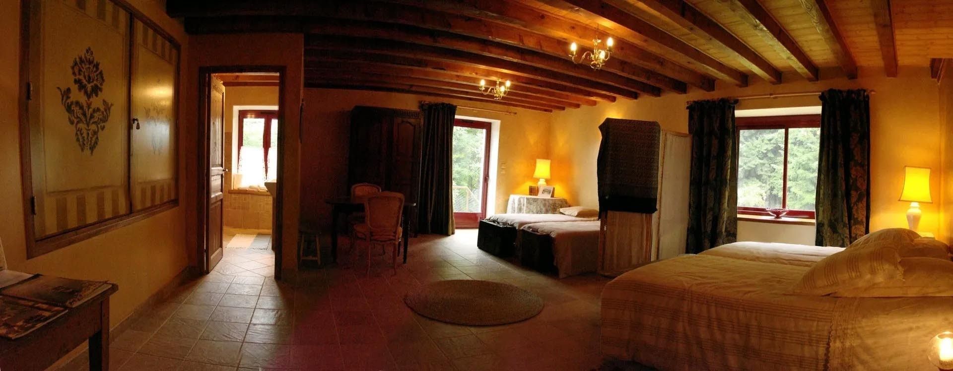 Een hotelkamer met een houten plafond, een bed, een bureau en een stoel. Er zijn twee ramen met gordijnen.