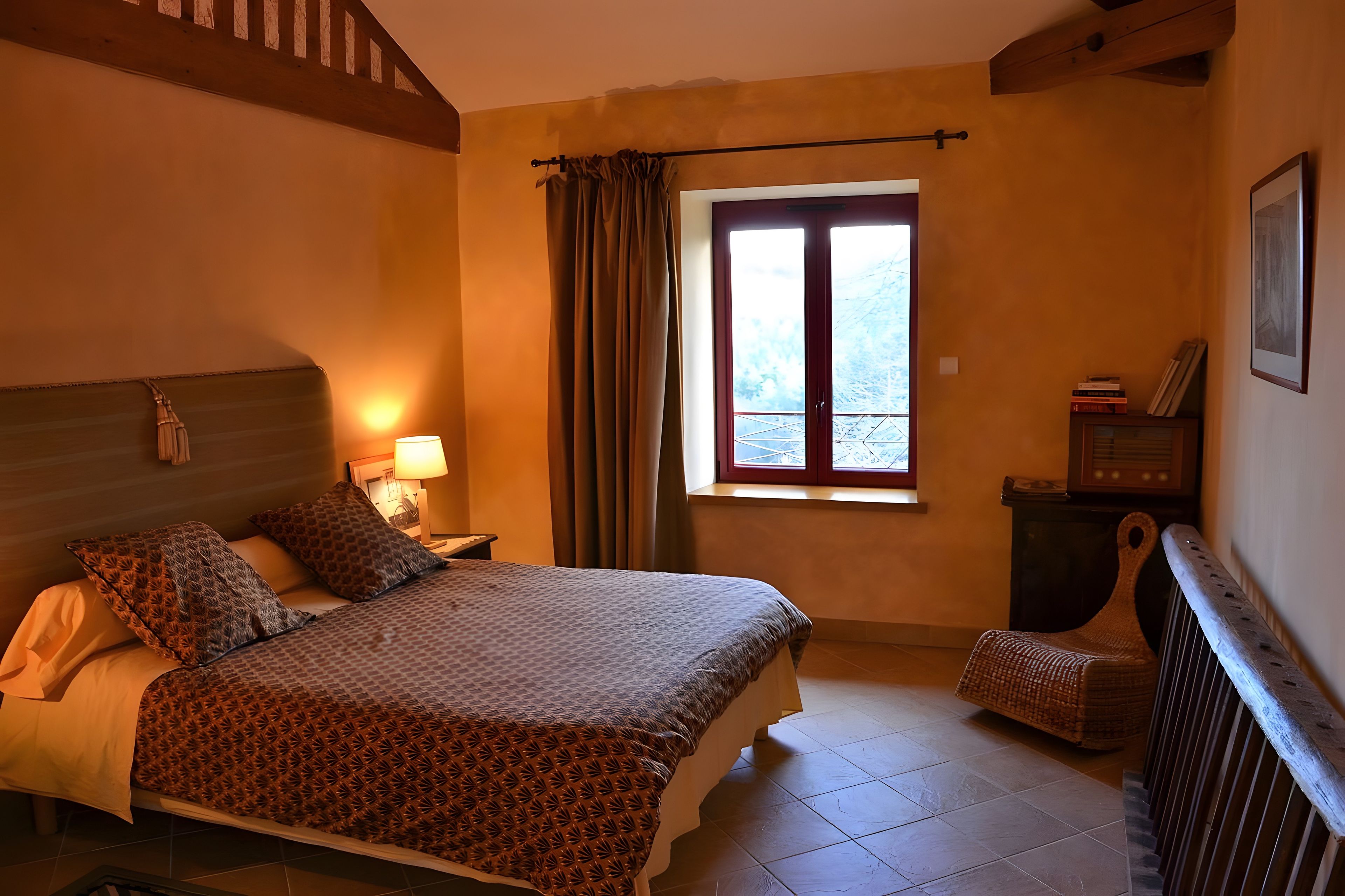 Ein Hotelzimmer mit Bett, Stuhl, Fenster mit Vorhängen, Nachttisch und Lampe.