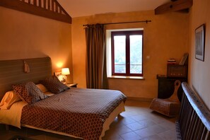 Une chambre d’hôtel avec un lit, une chaise, une fenêtre avec des rideaux, une table de chevet et une lampe.