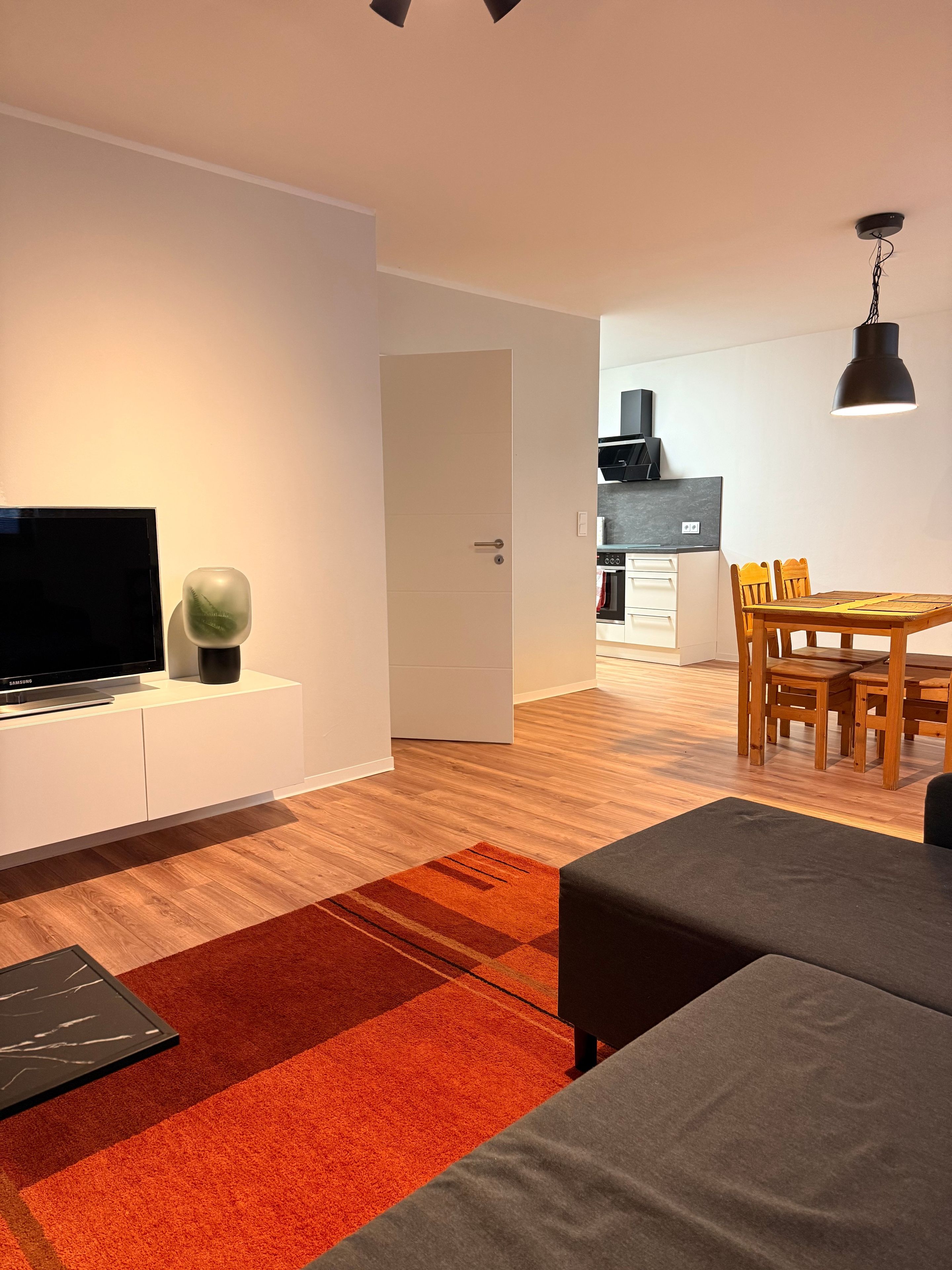 Ein modernes Wohnzimmer mit Flachbildfernseher, einer Couch und einem Essbereich mit Holztisch und Stühlen.