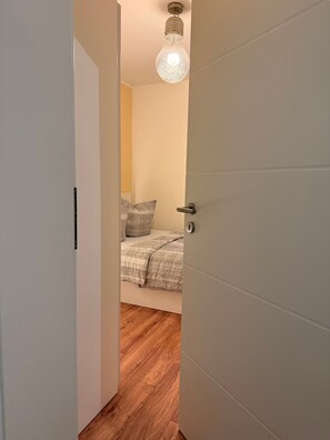Un pasillo estrecho que conduce a un dormitorio con una cama, una puerta y una lámpara.