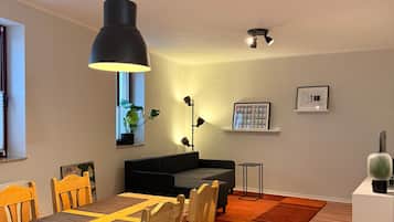 Ein Essbereich mit einem Holztisch, Stühlen, einer schwarzen Pendelleuchte und einem schwarzen Sofa im Hintergrund.