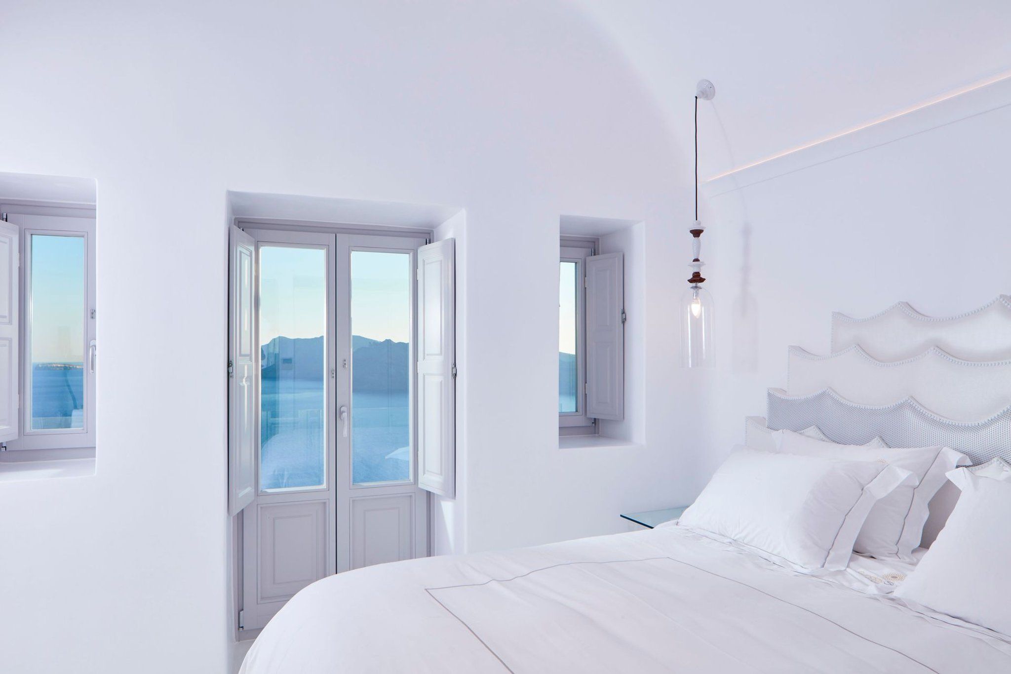 Une pièce blanche avec un lit, une fenêtre et une vue sur la mer.