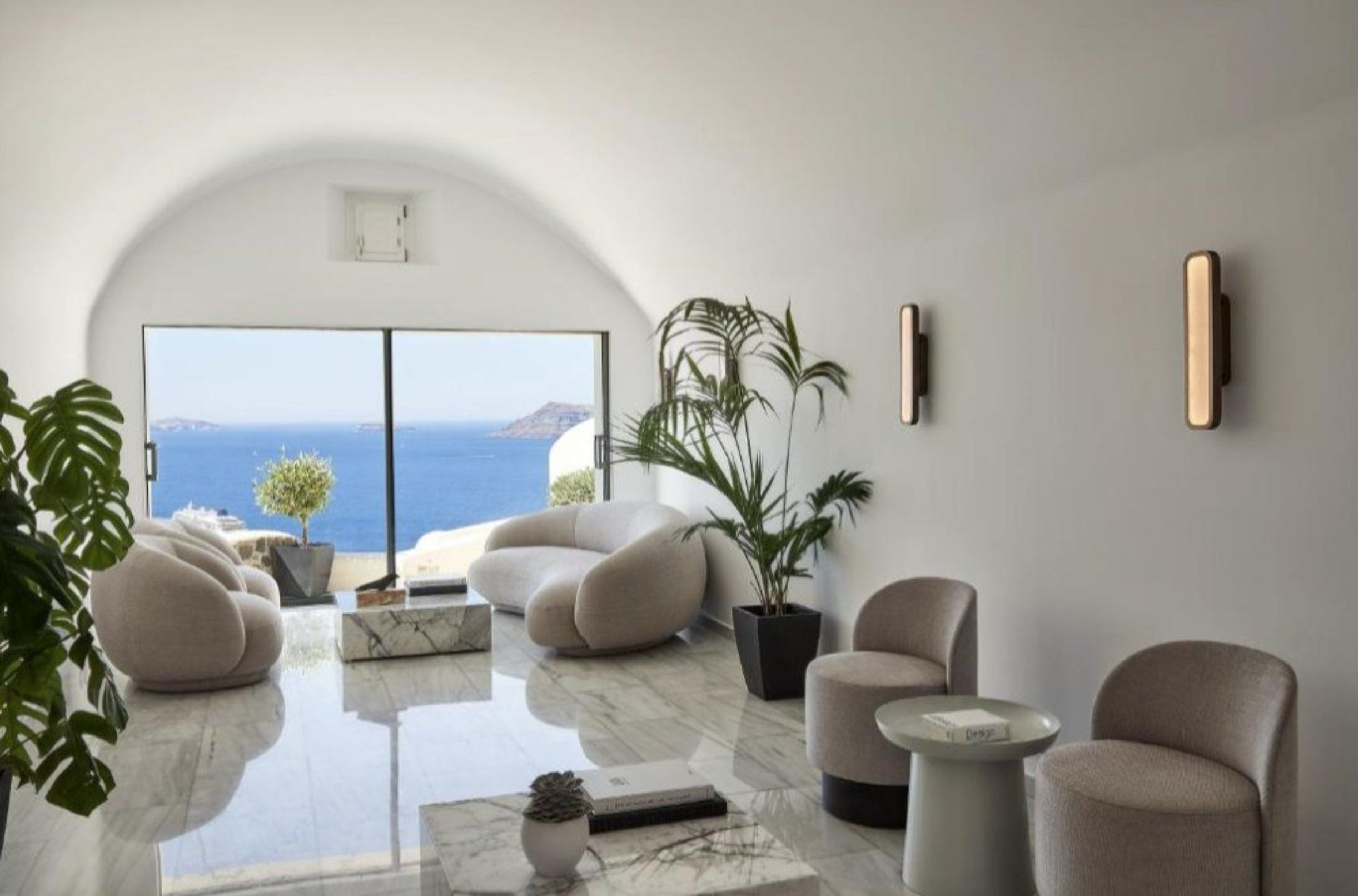 Un salon moderne doté d’une grande porte vitrée donnant sur un balcon avec vue sur la mer. On y trouve plusieurs canapés et une table basse.