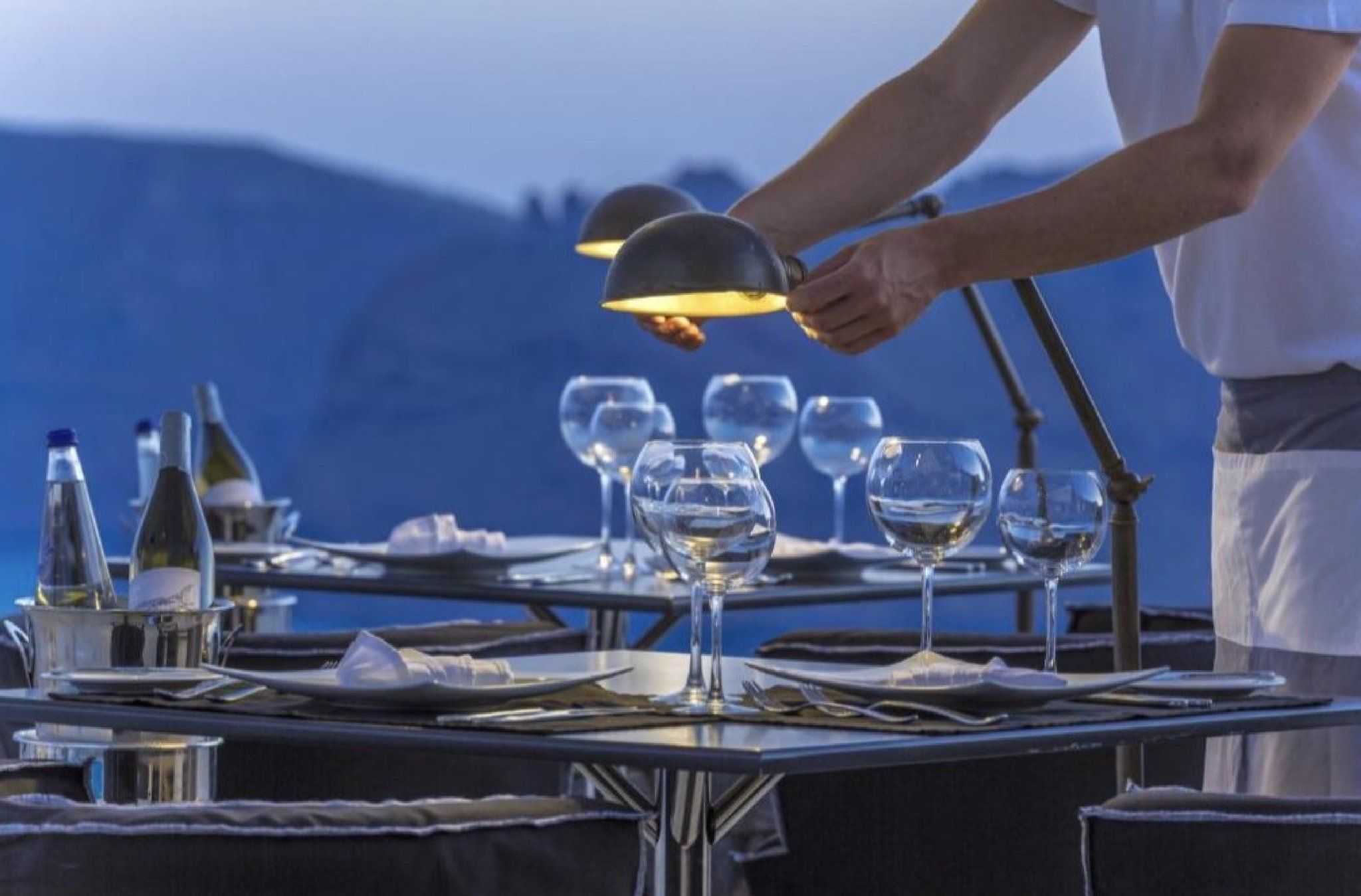 Une personne prépare une table en y disposant des verres à vin et des bouteilles, probablement pour un repas ou un événement.