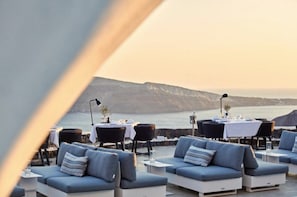 Eine Seeterrasse mit Sitzgelegenheiten und Tischen im Freien, mit Blick auf ein Gewässer und sanfte Hügel in der Ferne.