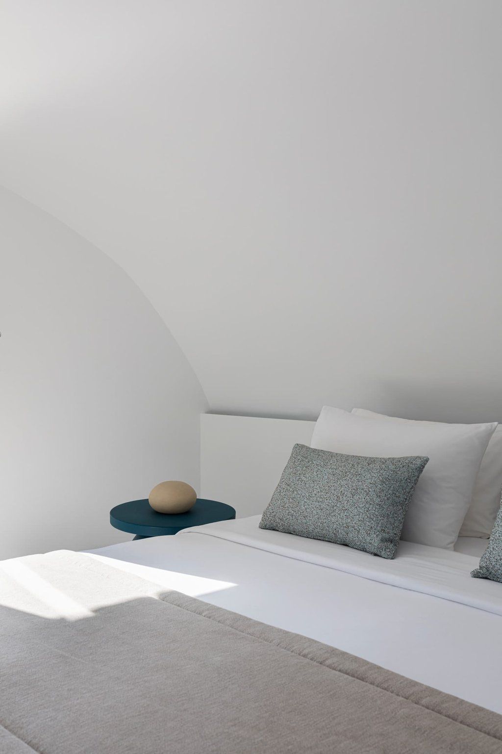 Une chambre à coucher avec un lit, des oreillers, un objet rond posé sur un socle bleu et un mur blanc.