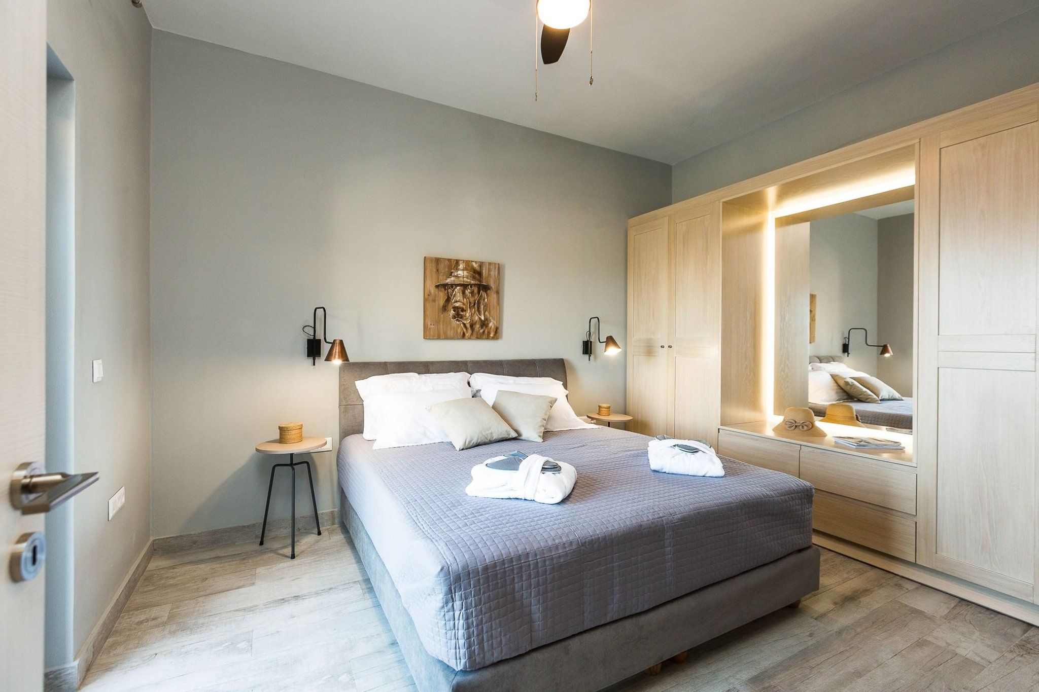 A modern bedroom with a large bed, bedside lamps, a wooden headboard, and a mirror.
