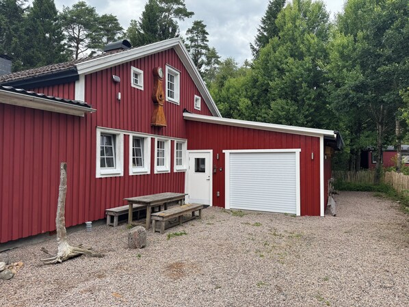 Een rood gebouw met een witte garage deur, een houten bank en een houten constructie die op een klok lijkt.