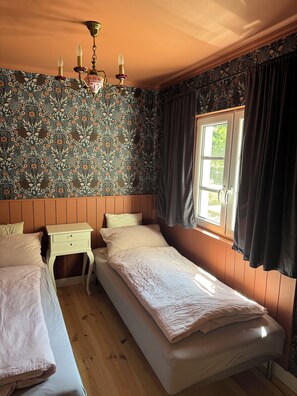 Ein Schlafzimmer mit einem Einzelbett, einem Nachttisch, einem Fenster mit Vorhängen und einem gemusterten Wandpapier.