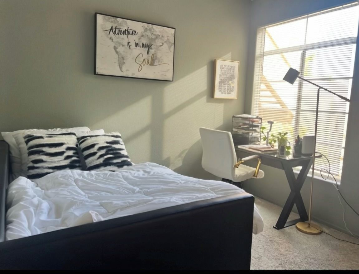 A bedroom with a bed, a desk, and a window.