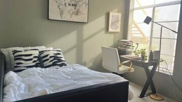 A bedroom with a bed, a desk, and a window.