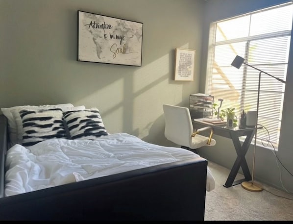 A bedroom with a bed, a desk, and a window.