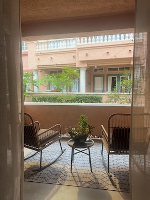 A balcony with two wicker chairs, a small table, and a potted plant.