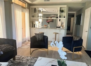 A living room with two sofas, a coffee table, and a kitchen area with shelves and a counter. - Luxury Designer Tulum-African Craftsman Get-Away (Oceanside)