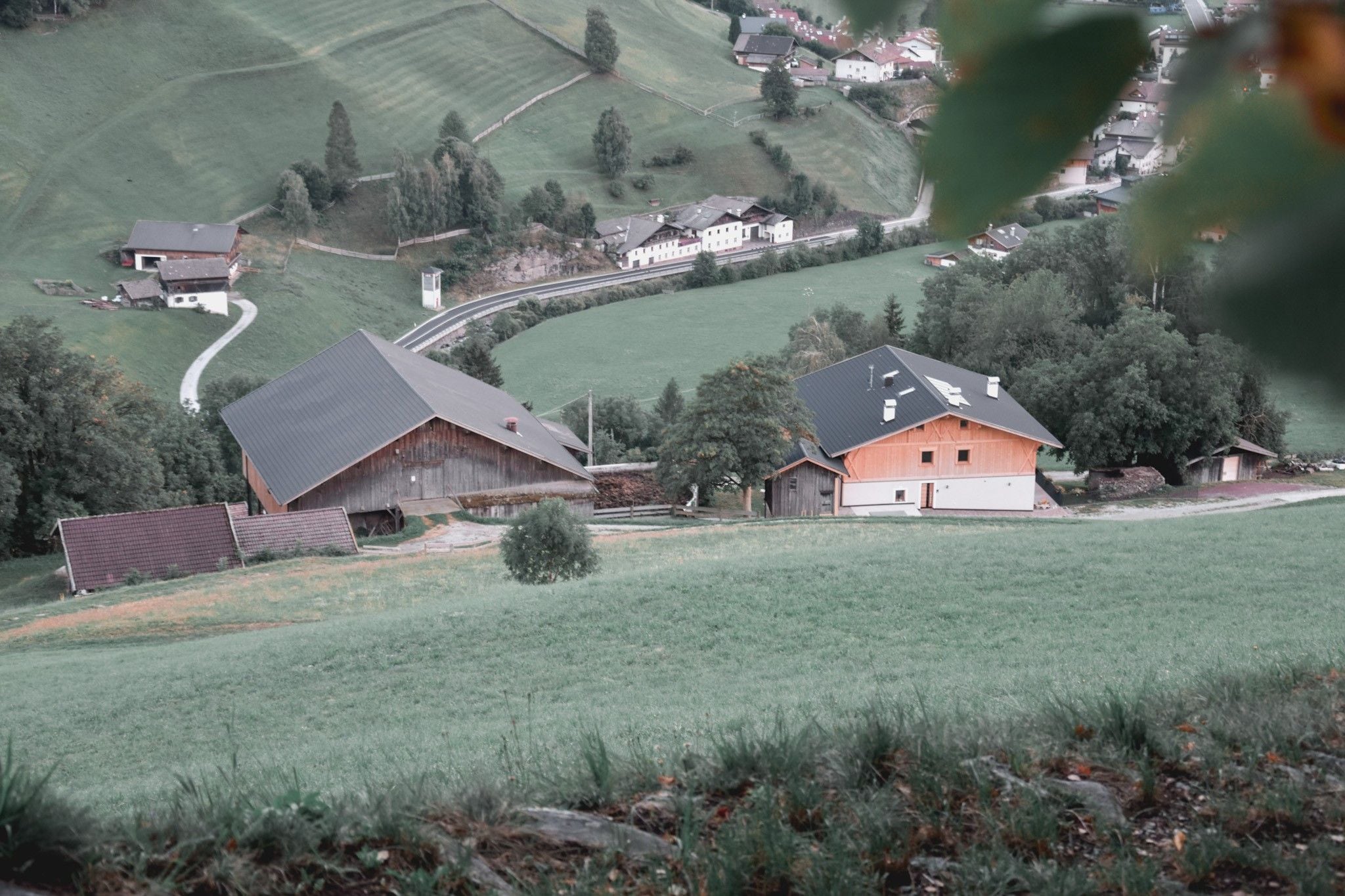 A rural landscape with a winding road, a barn, and a house with a sloped roof.