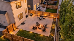 Un patio trasero con una fogata y zona de estar, rodeado por una valla de madera y una casa.