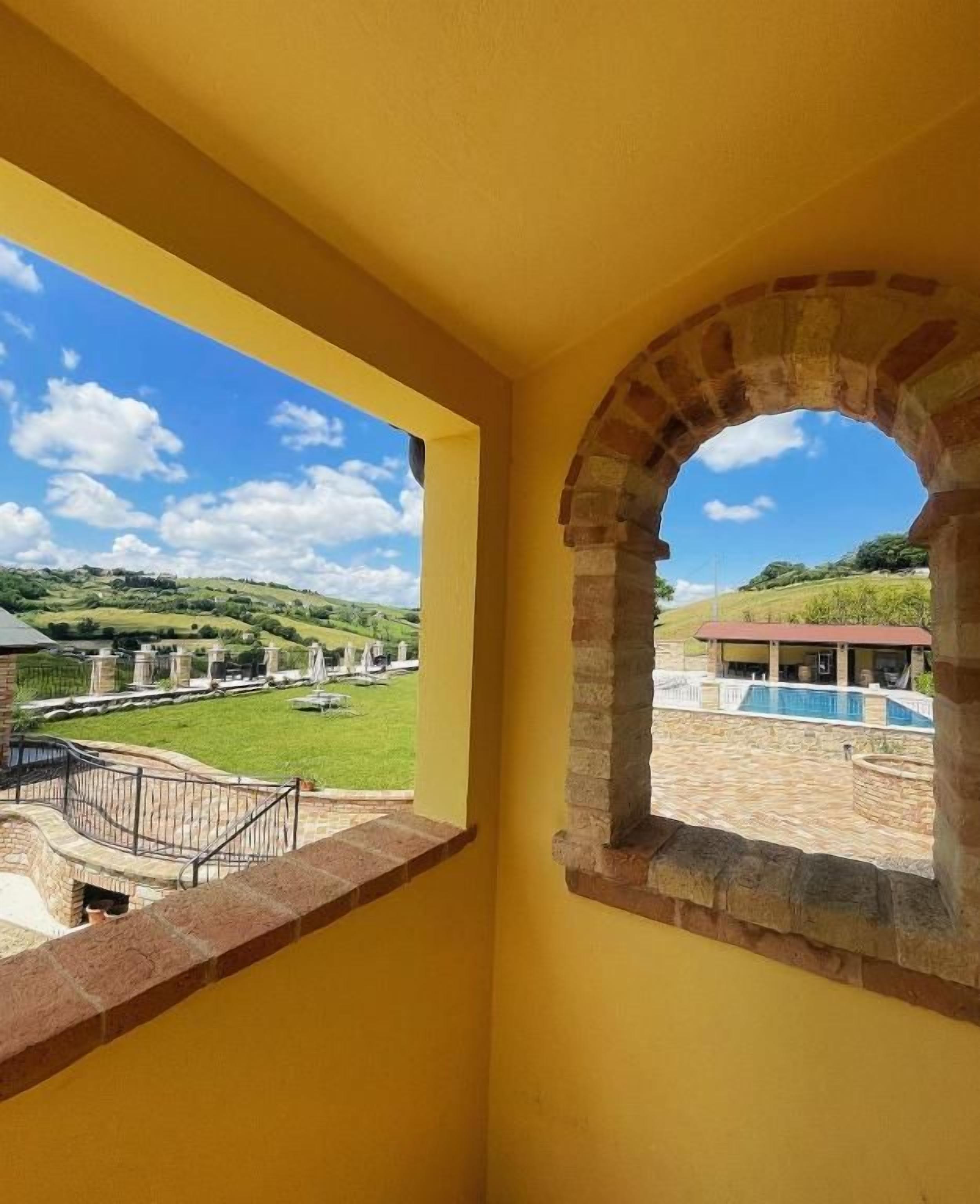 Un balcon aux murs jaunes, offrant une vue sur une piscine et un paysage verdoyant.