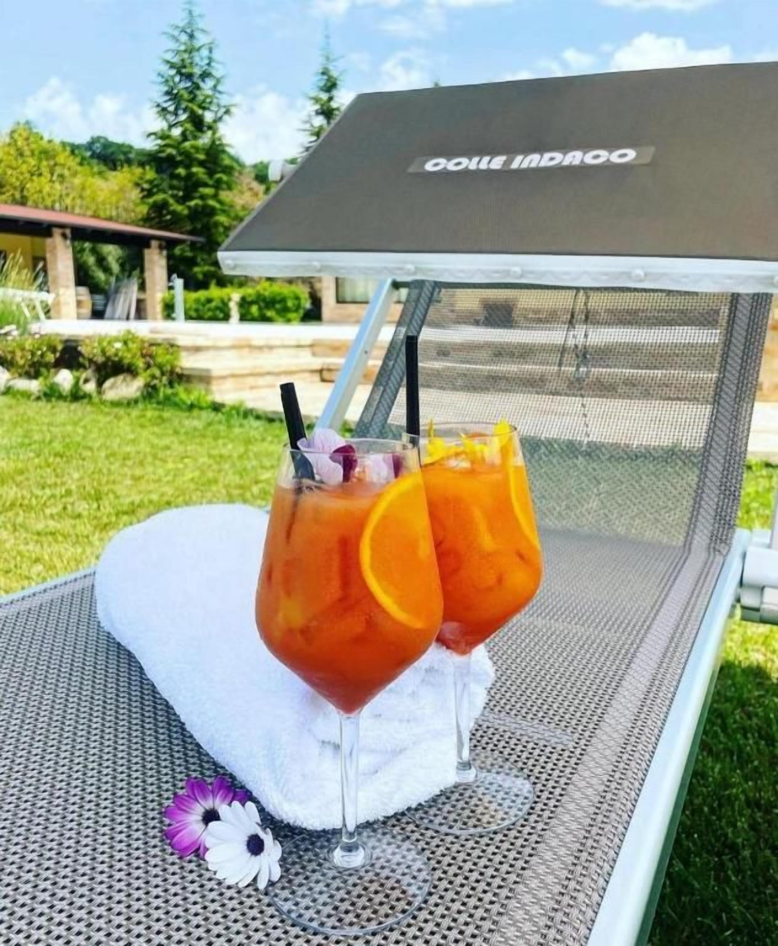 Two glasses of iced beverage with orange slices on a mesh chair outdoors.