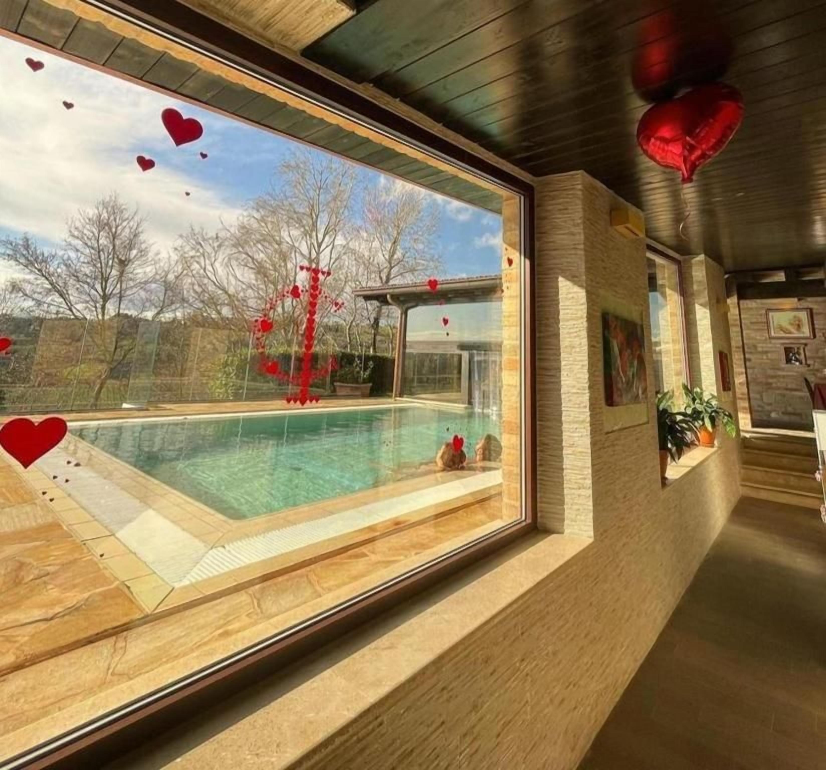 A modern interior with a large window overlooking a swimming pool, a wooden ceiling, and a stone wall.
