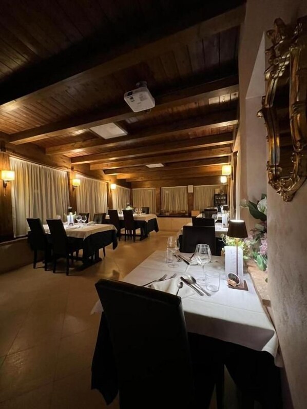 A restaurant with wooden ceiling beams, tables set for dining, and wall-mounted sconces.