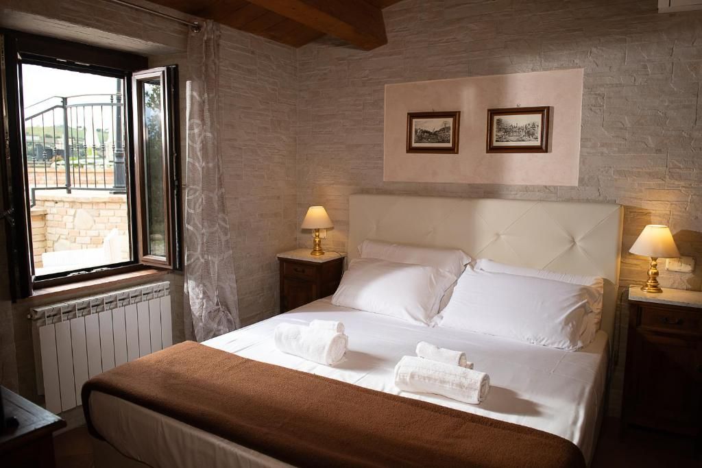 Una habitación de hotel con cama, dos lámparas de noche, un ventanal con cortinas, un radiador y dos cuadros en la pared.