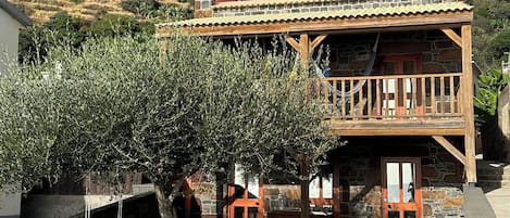 A stone building with a wooden balcony, a swing, and a small garden with a tree.