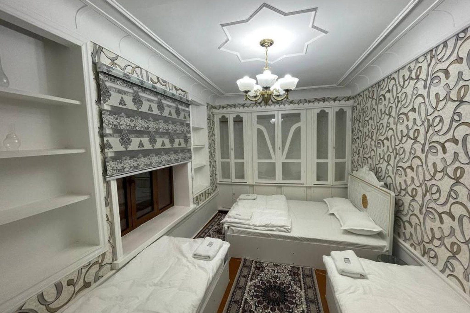 Una habitación con cama, ventana, candelabro y paredes con diseño.