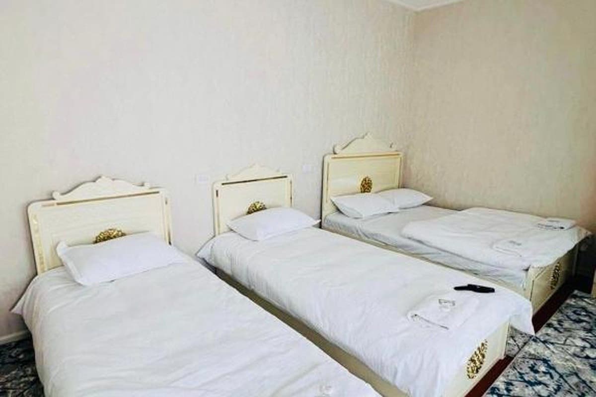 A room with three single beds aligned against a wall, each with a white bedspread and a headboard with a decorative element.