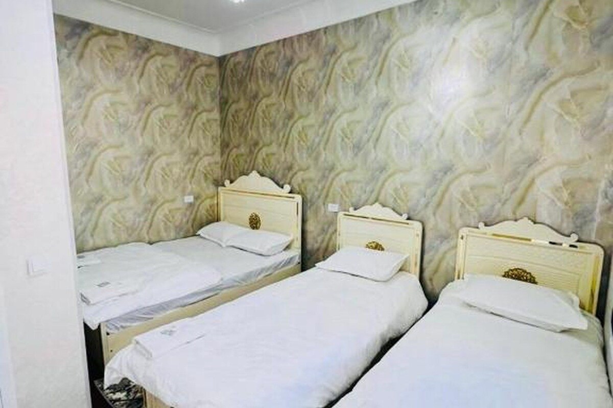 A room with two single beds, each with a wooden headboard and white bedding. The walls have a textured, marble-like pattern.