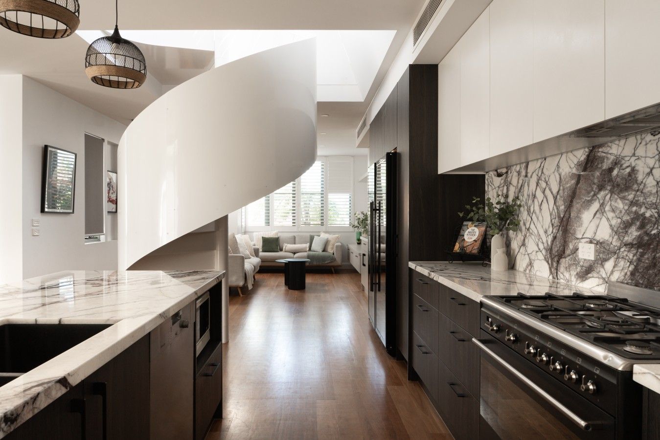 Een moderne keuken met een rond keukenblok, donkere kastjes en een marmeren spatwand.