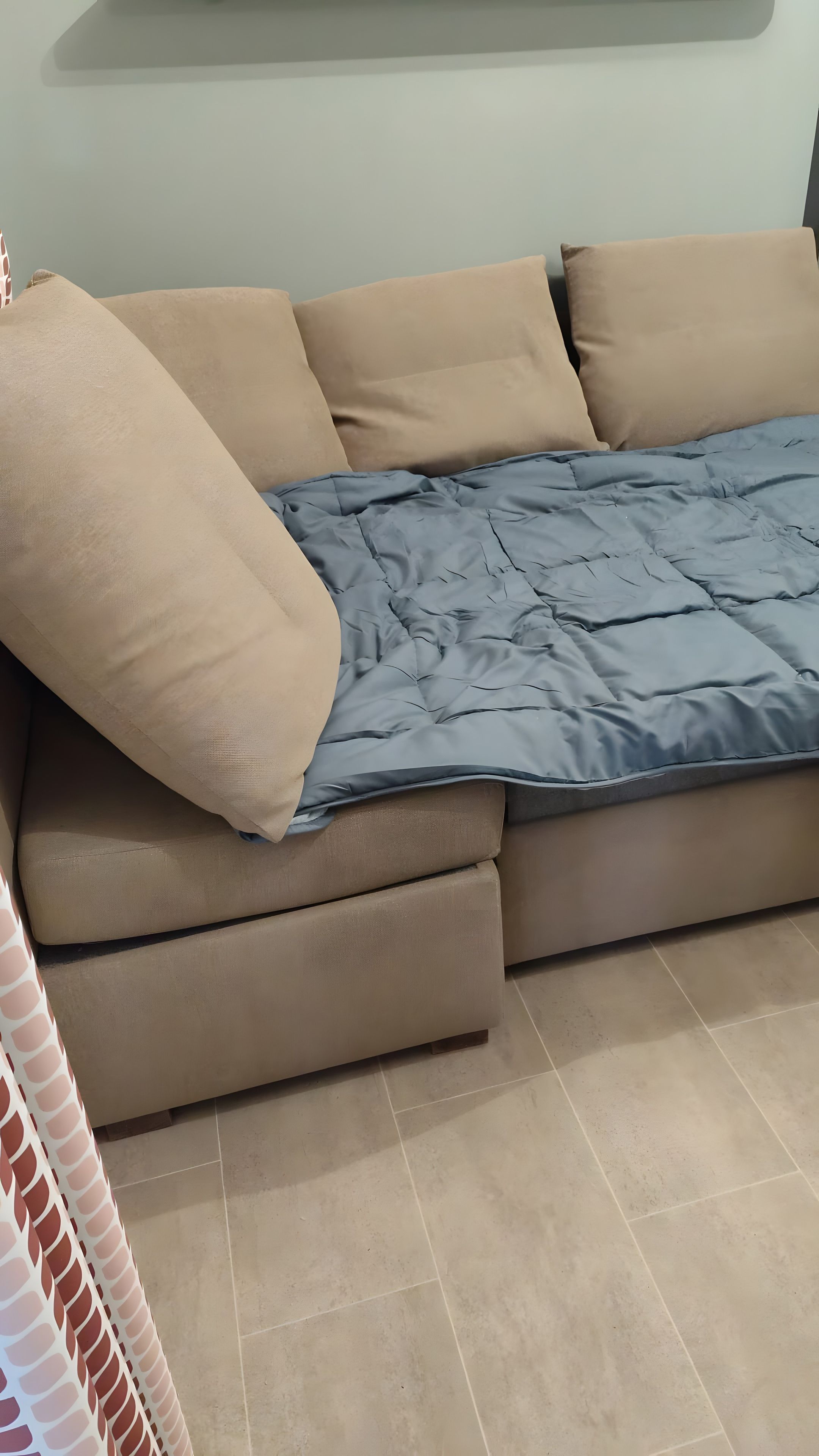 Een bank met een blauwe hoes en beige kussens, staand op een betegelde vloer.