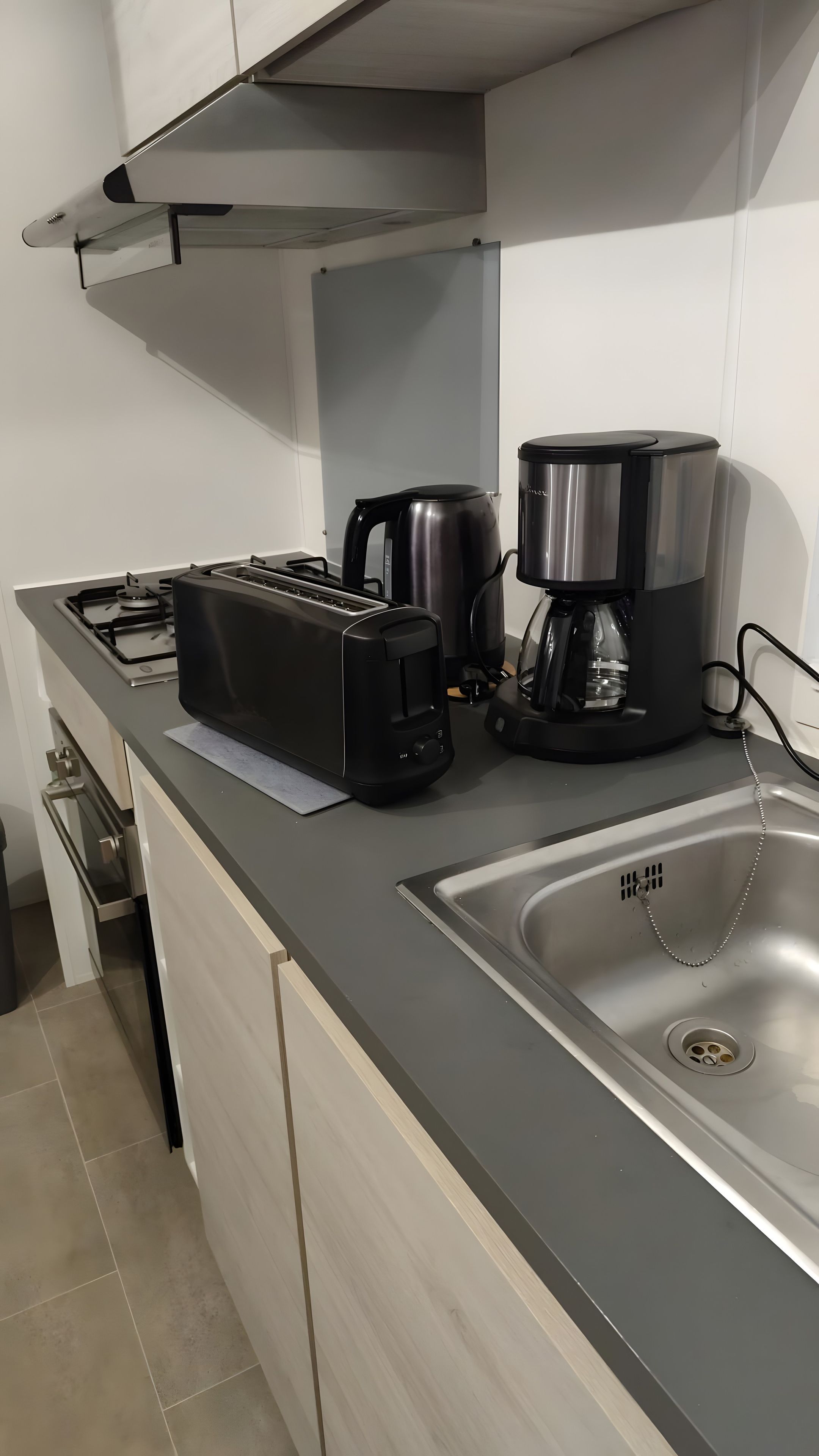 Et moderne køkken med gasblus, brødrister, kaffemaskine og en stålvask.