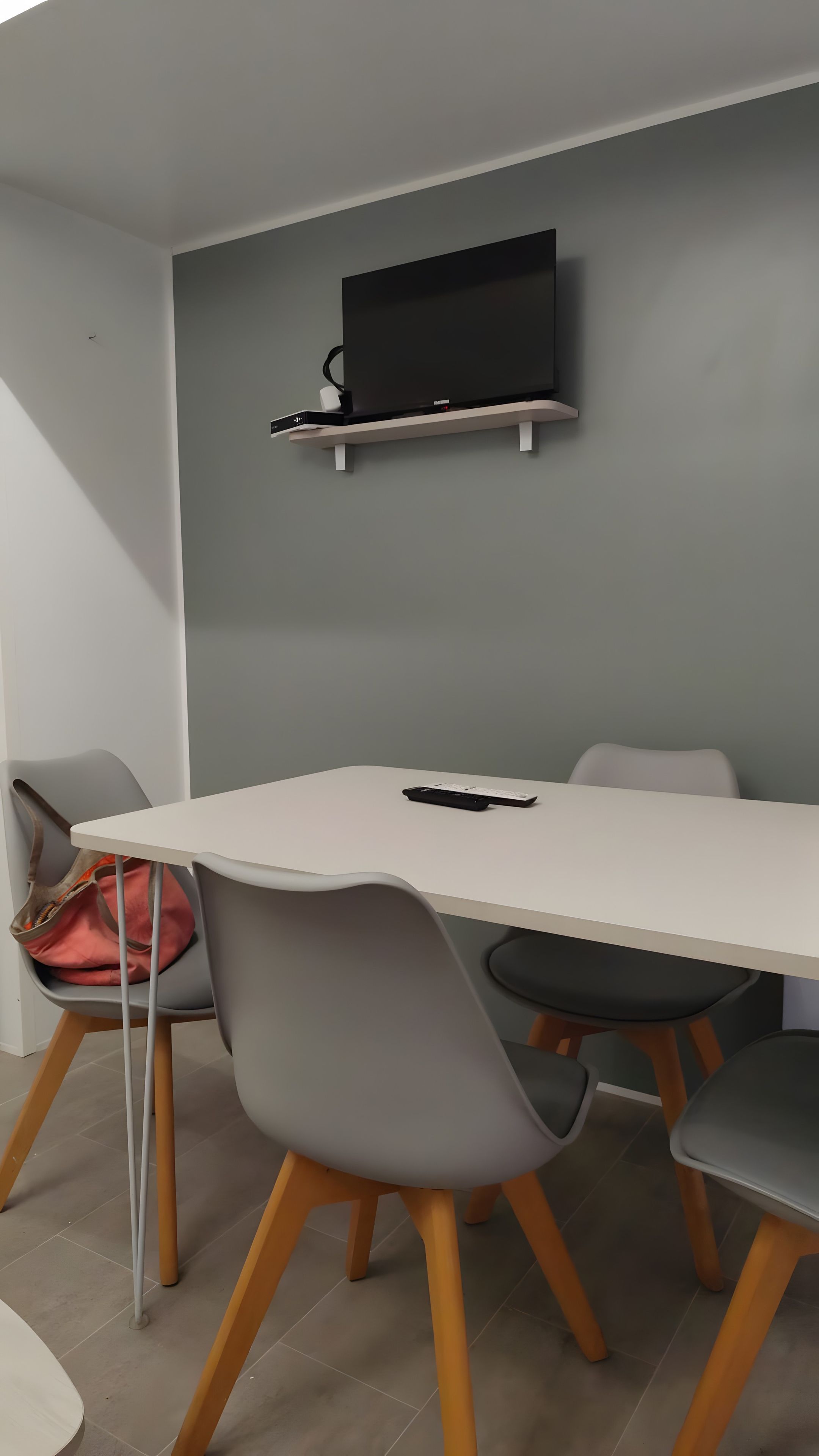 Et moderne spiseområde med et hvidt bord, grå stole og et ophængt fjernsyn på væggen.