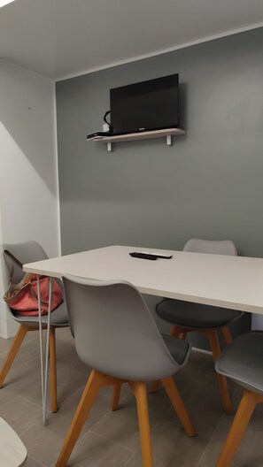 Et moderne spiseområde med et hvidt bord, grå stole og et ophængt fjernsyn på væggen.