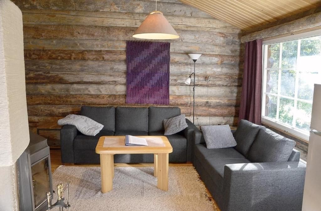 A cozy living room with a fireplace, a sofa set, a coffee table, and a large window with curtains.