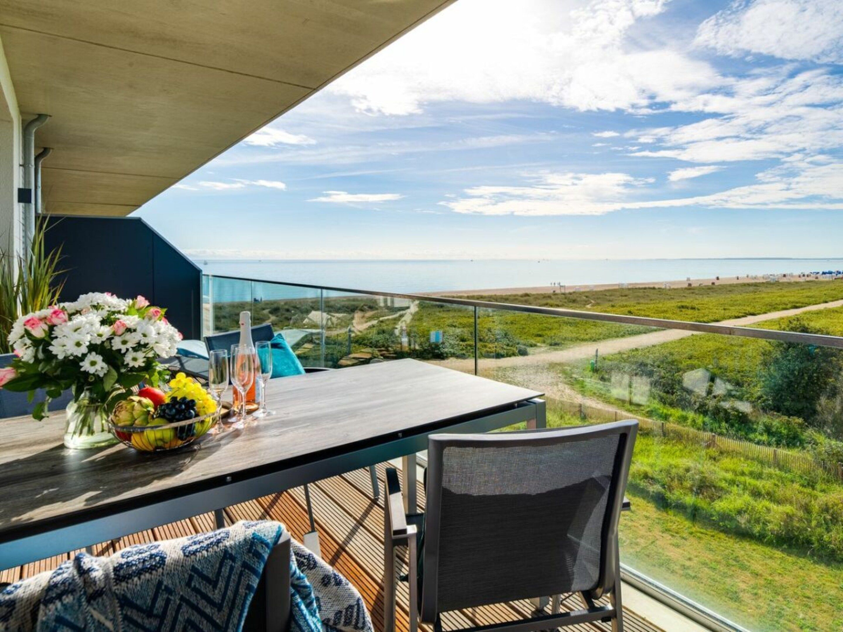 A balcony with a table set for dining, a chair, and a view of the beach and landscape.