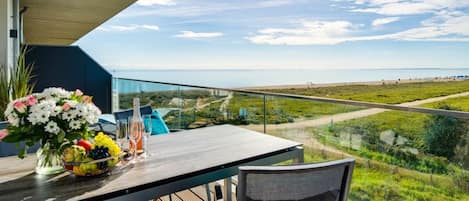 A balcony with a table set for dining, a chair, and a view of the beach and landscape.