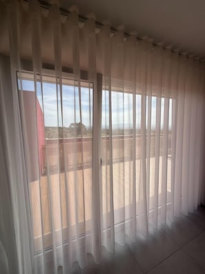 Habitació amb grans finestres vistes a un edifici vermell i un cel blau.