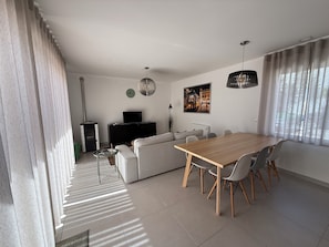 Un saló modern amb zona de menjador, que inclou un sofà, una taula de dinar de fusta i una televisió.