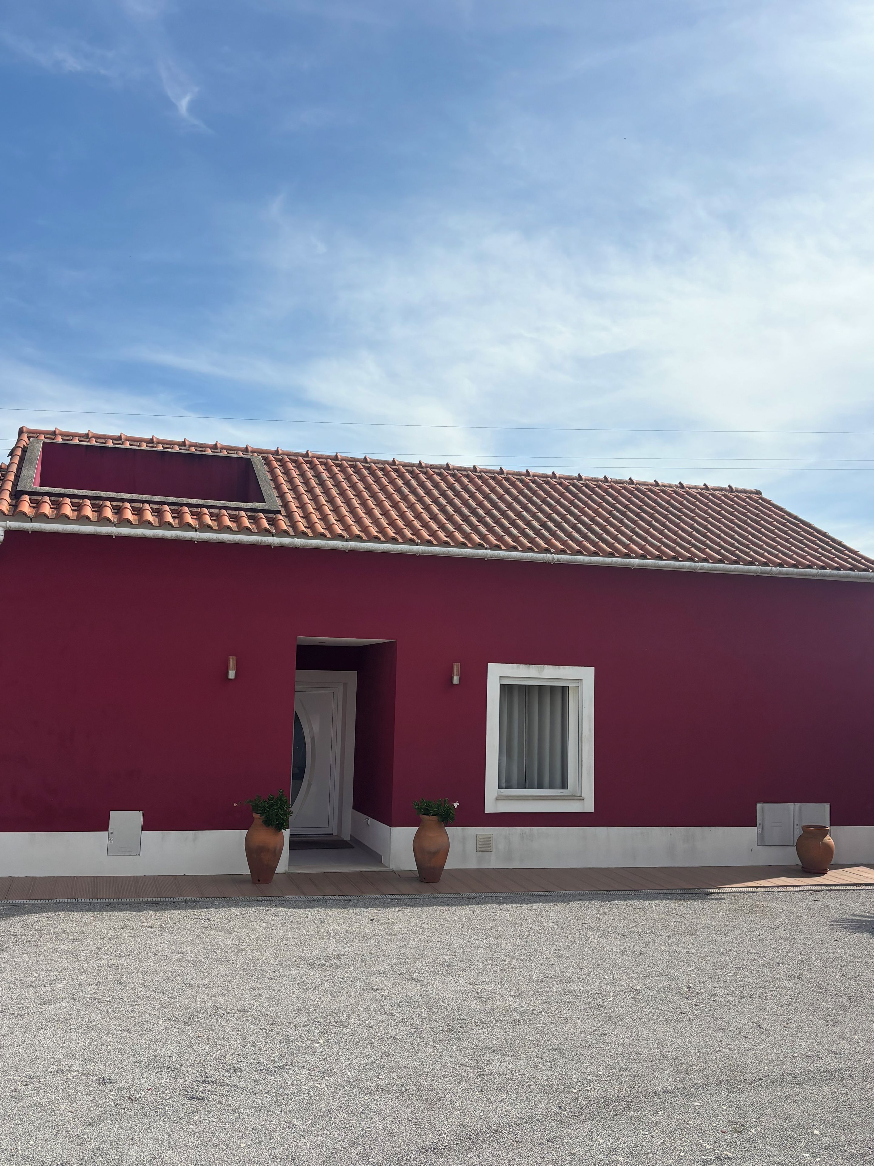 A building with a red facade, a tiled roof, and two potted plants in front.