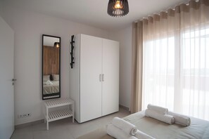 A bedroom with a bed, a wardrobe, a bench, a mirror, and a window with curtains.
