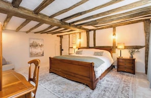 A bedroom with a wooden bed, a nightstand, a chair, and a table. - Luxurious 7 bed Tudor Country Retreat nestled in West Sussex woodland (Crawley)